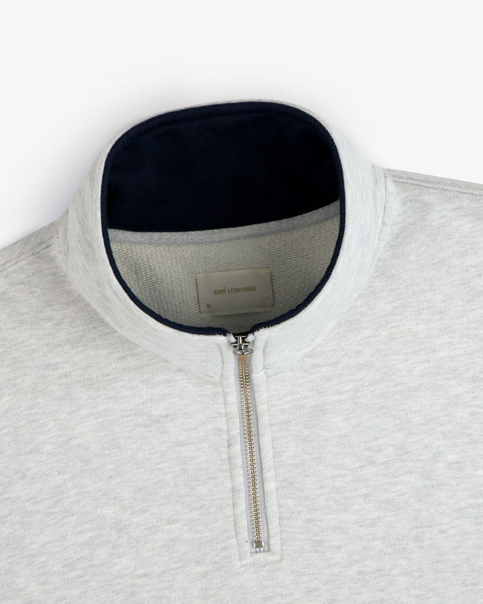 Aimé Souvenir Quarter Zip in light grey with silver zipper and dark collar lining, laid flat on a white background.