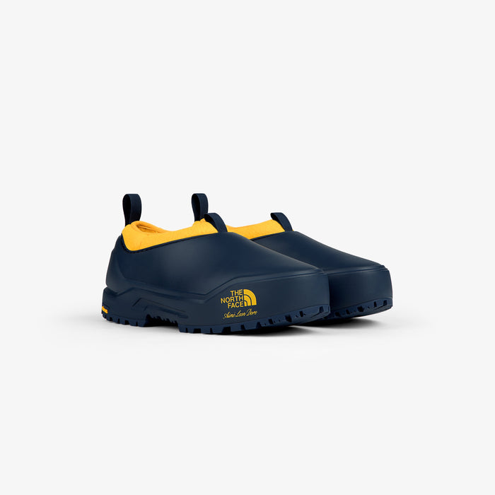 ALD / The North Face Base Camp Mule: navy blue slip-ons with yellow lining, logo on side, white background.
