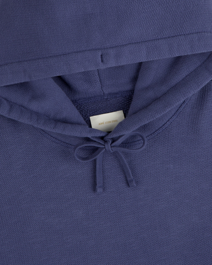 Close-up of the Stone Washed Marina Hoodie, blue with a bow-tied drawstring and a white label inside the collar.