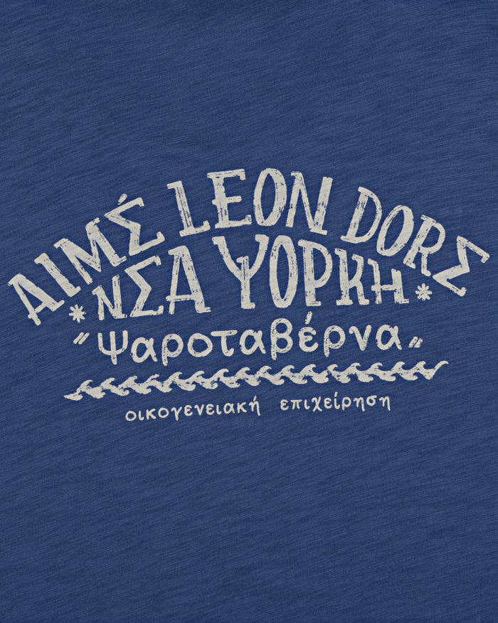 The Taverna Tee features blue fabric with white Greek and English text in a handwritten style.