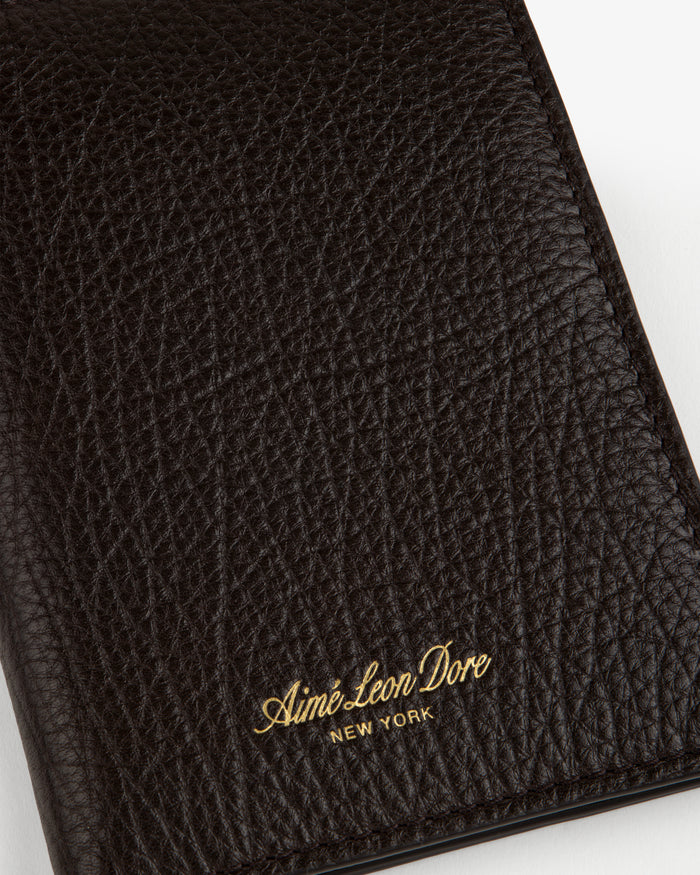 Close-up of a textured black Tumbled Leather Passport Holder with Aimé Leon Dore NEW YORK in gold lettering.